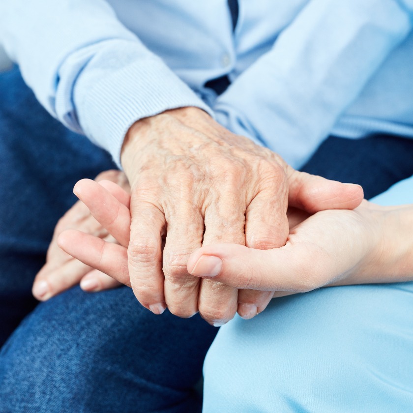 Altenpfleger hält tröstend Hand einer alten Frau